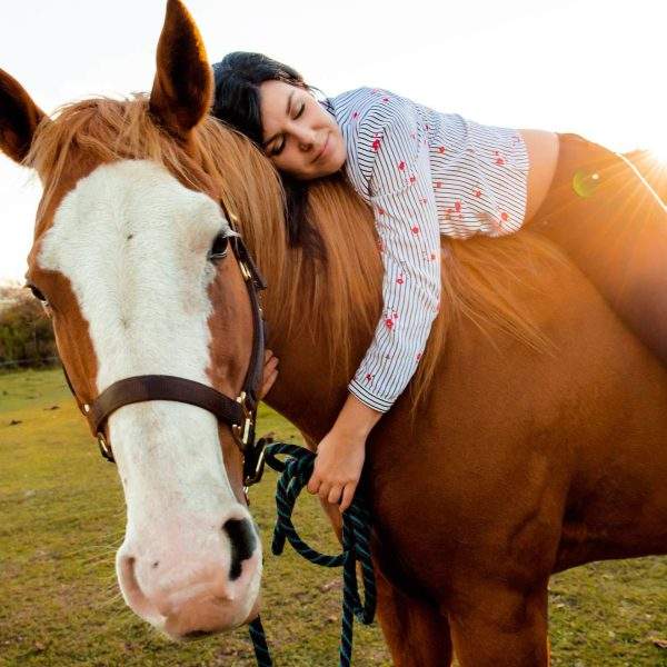 A girl hugging her horse while laying on top of it.